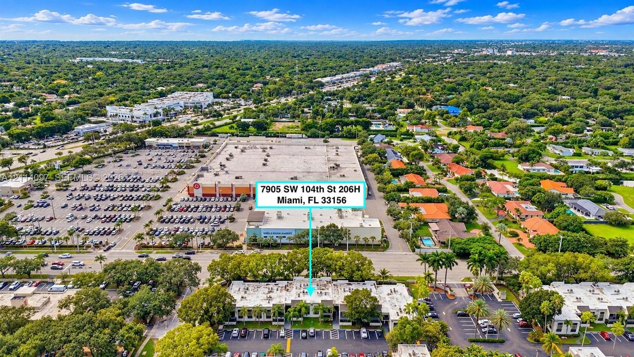Aerial perspective of a multi-unit complex featuring exterior parking areas, low-rise architecture, and mature trees situated in a developed urban area