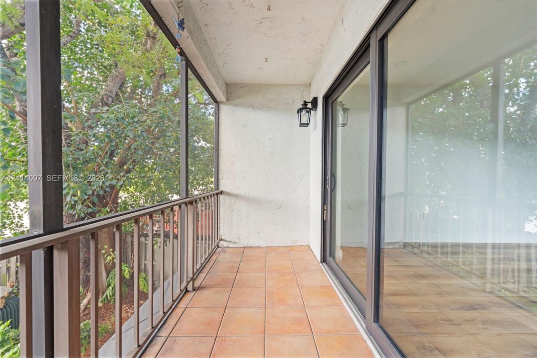 Screened-in balcony featuring tile flooring, metal railings, and a wall-mounted light fixture