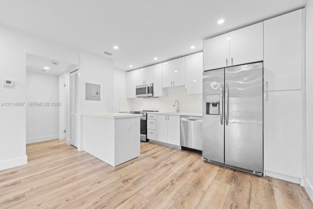 Kitchen featuring white high-gloss cabinetry, stainless steel appliances, wood-finish flooring, quartz countertops, and recessed lighting
