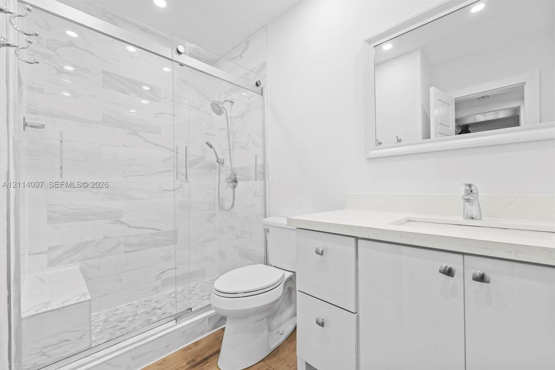 Bathroom featuring a walk-in shower with glass sliding doors, built-in tiled bench, stone-patterned wall tile, vanity with a light-toned countertop, and wood-finish flooring
