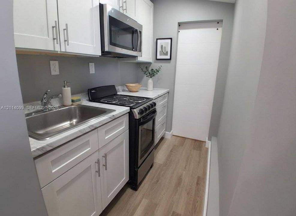 Kitchen featuring white shaker-style cabinetry, stone-finish countertops, stainless steel appliances, a stainless steel sink, and wood-finish flooring
