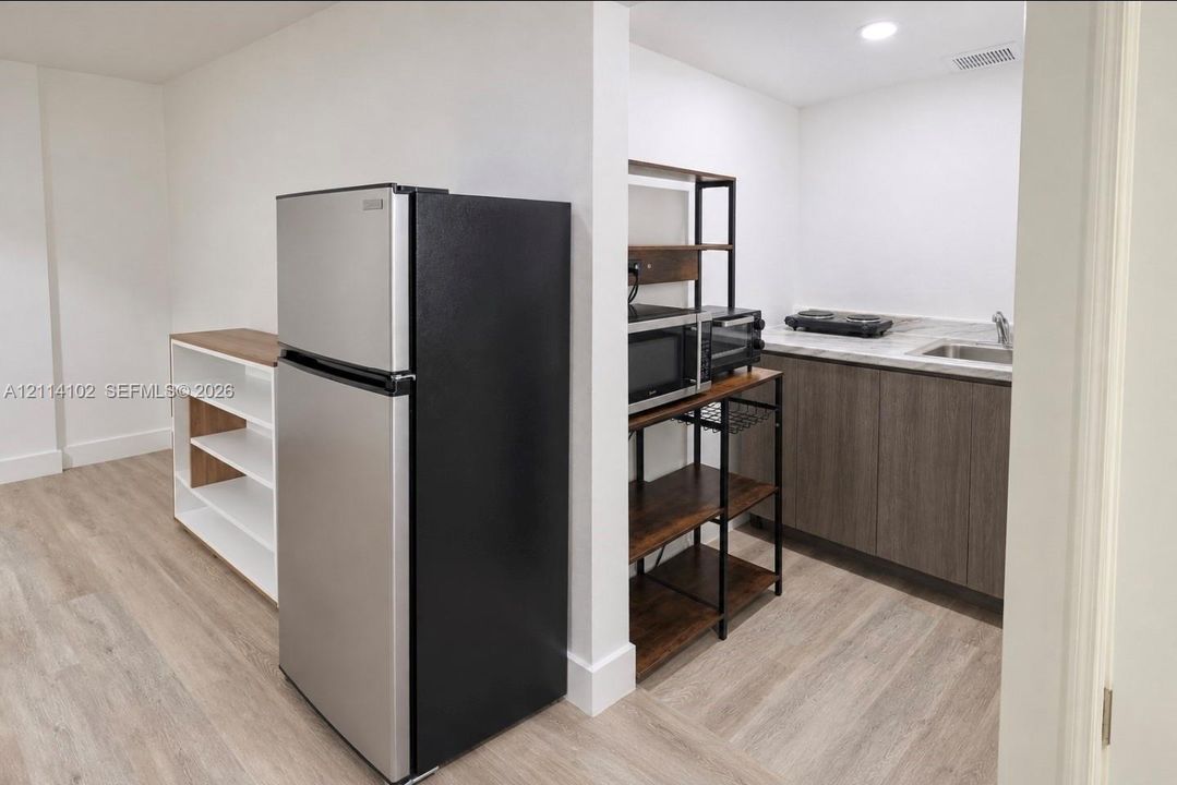 Kitchenette featuring wood-finish flooring, stone-surfaced countertop, stainless steel sink, and flat-panel cabinetry
