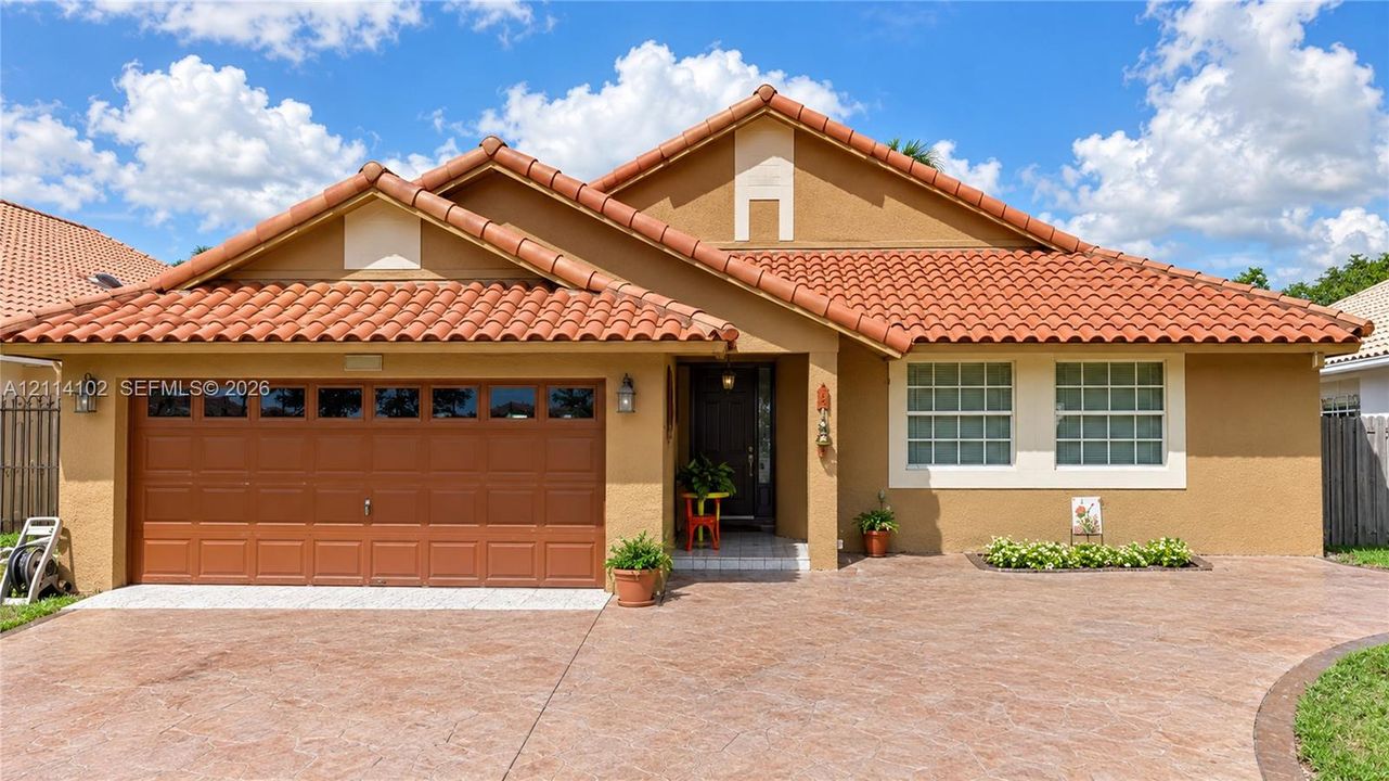 Single-story residence featuring a terracotta-tiled roof, textured stucco facade, stamped concrete driveway, two-car garage, and grid-pattern window panes