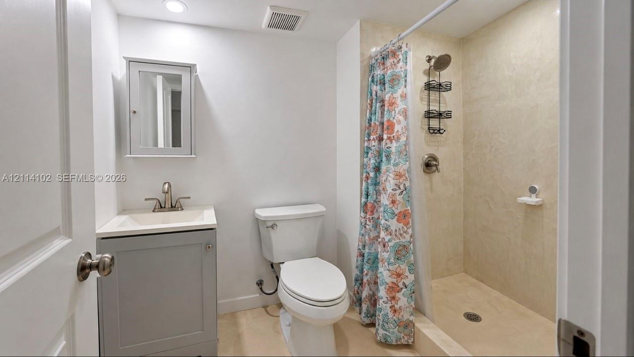 Bathroom featuring a gray shaker-style vanity, a recessed medicine cabinet, a chrome faucet, and a walk-in shower with integrated tile surround