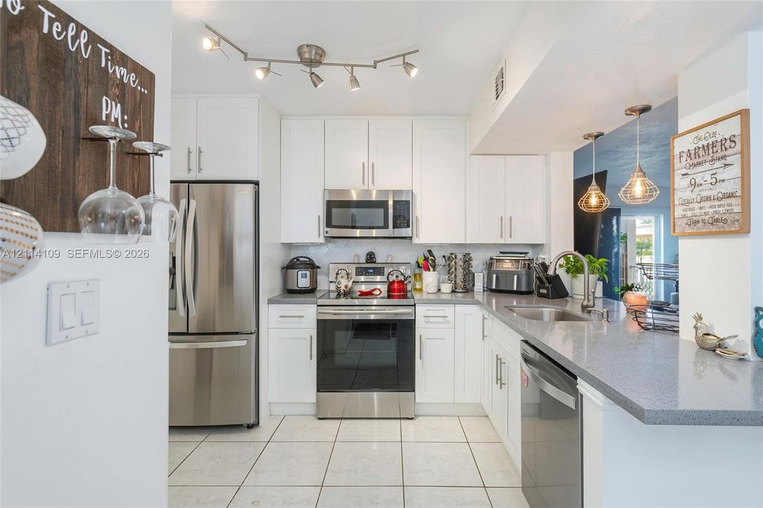 Kitchen featuring white shaker-style cabinetry, stainless steel appliances, grey solid-surface countertops, tile flooring, and adjustable track lighting