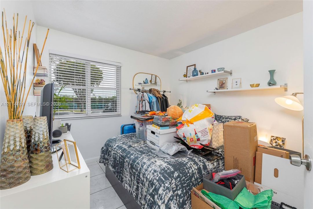 Interior space featuring white tile flooring, horizontal window blinds, and two white wall-mounted floating shelves