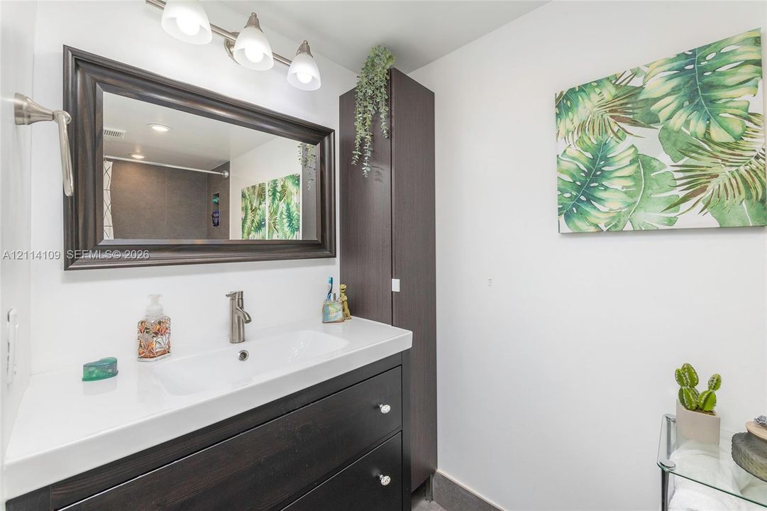Bathroom vanity featuring dark wood-finish cabinetry, white countertop, integrated rectangular sink, brushed nickel faucet, and matching framed mirror with three-light fixture