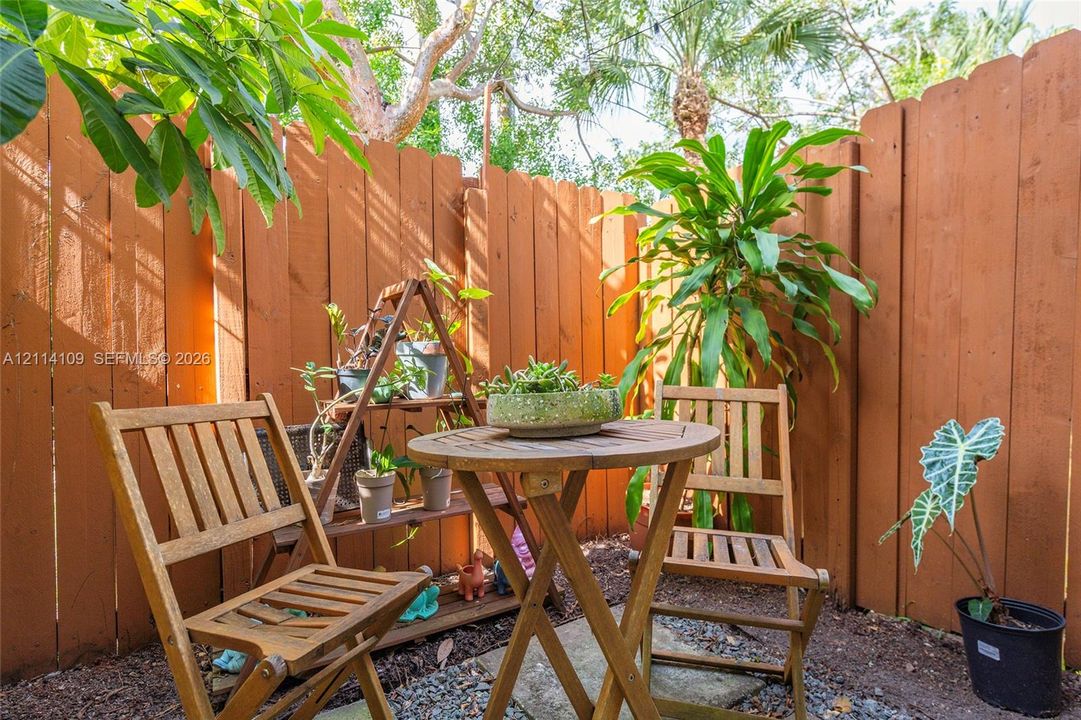 Private outdoor area enclosed by a vertical wood-plank fence, featuring a ground-level stone paver base and organic wood-mulch surfacing