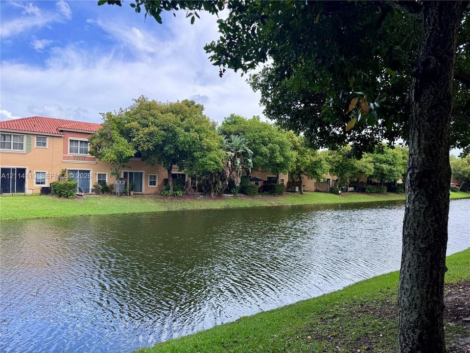Waterfront exterior featuring a terracotta-tile roof, stucco facade, sliding glass doors, and expansive green space with mature trees