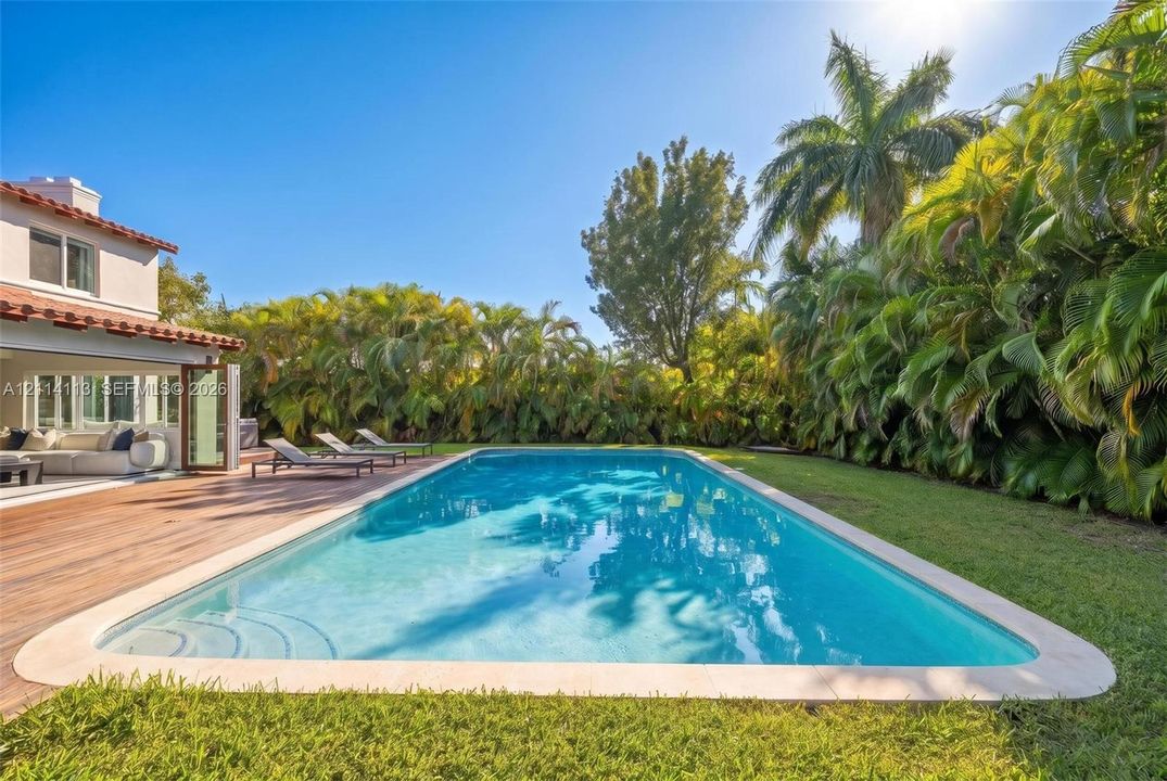 In-ground swimming pool with a stone coping border, wood-finish decking, and extensive perimeter greenery