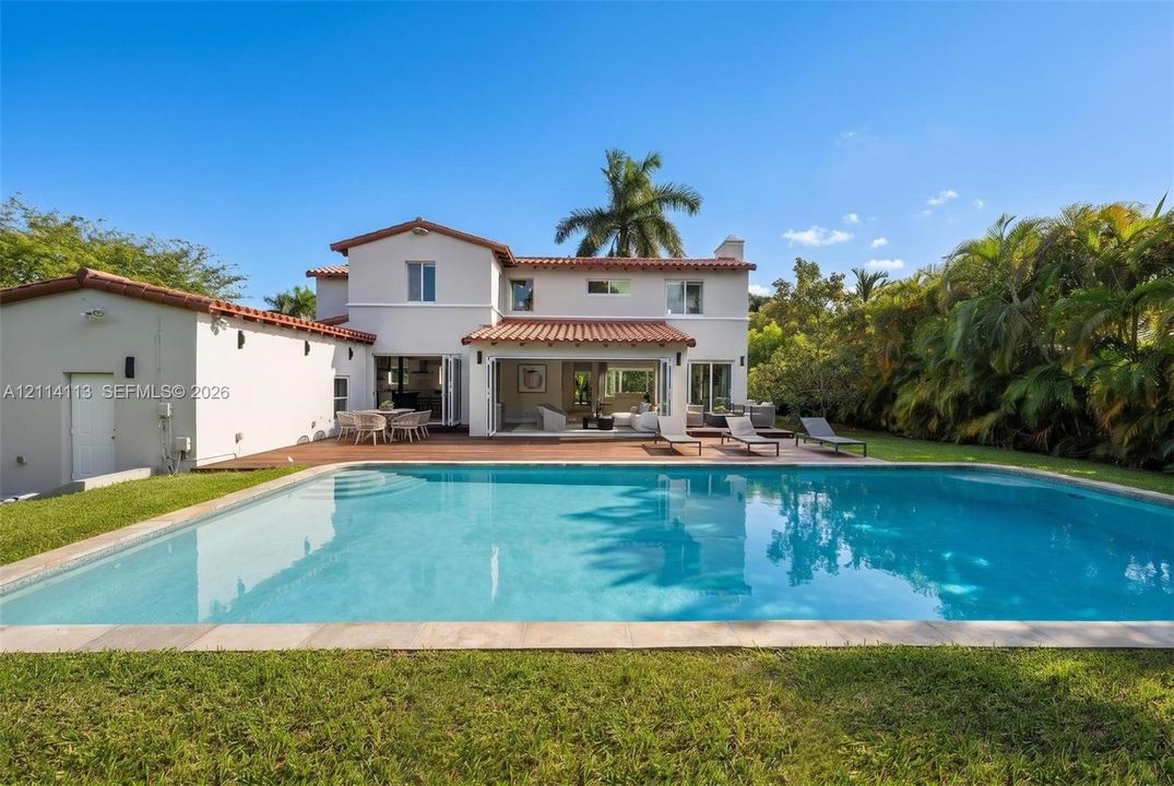 Two-story residence featuring a tile roof, an in-ground swimming pool, a wood-decked patio, and exterior bi-fold glass doors