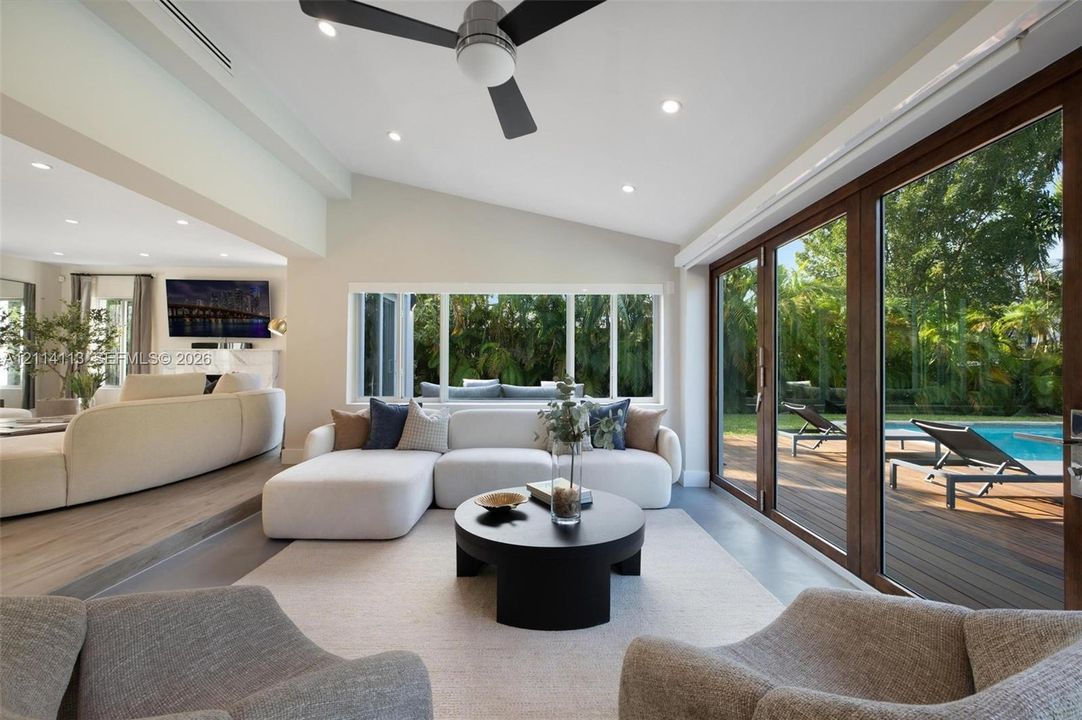 Living area featuring a vaulted ceiling, recessed lighting, wood-finish flooring, and expansive folding glass doors opening to the exterior deck