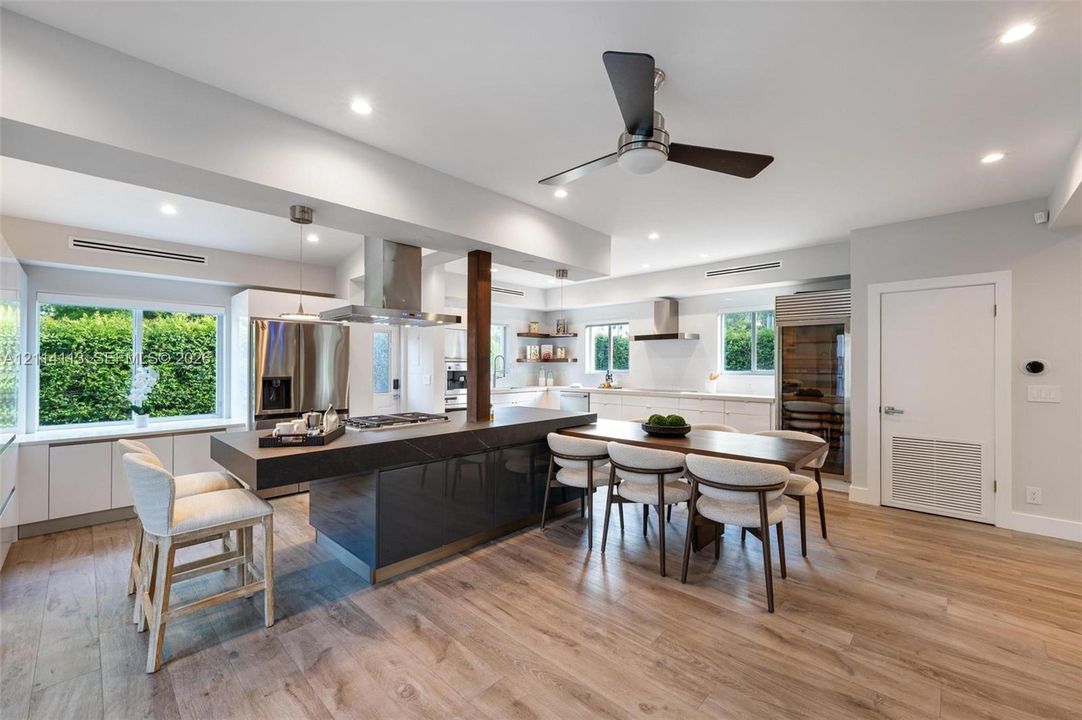 Gourmet kitchen featuring a large central island with stone-finish countertop, stainless steel appliances, wood-finish flooring, recessed lighting, and built-in wine storage