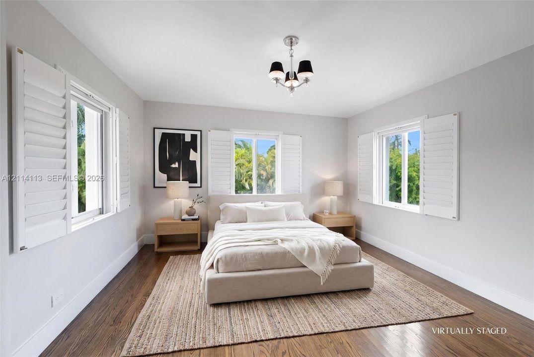 Light-filled room featuring wood-finish flooring, three windows with white plantation shutters