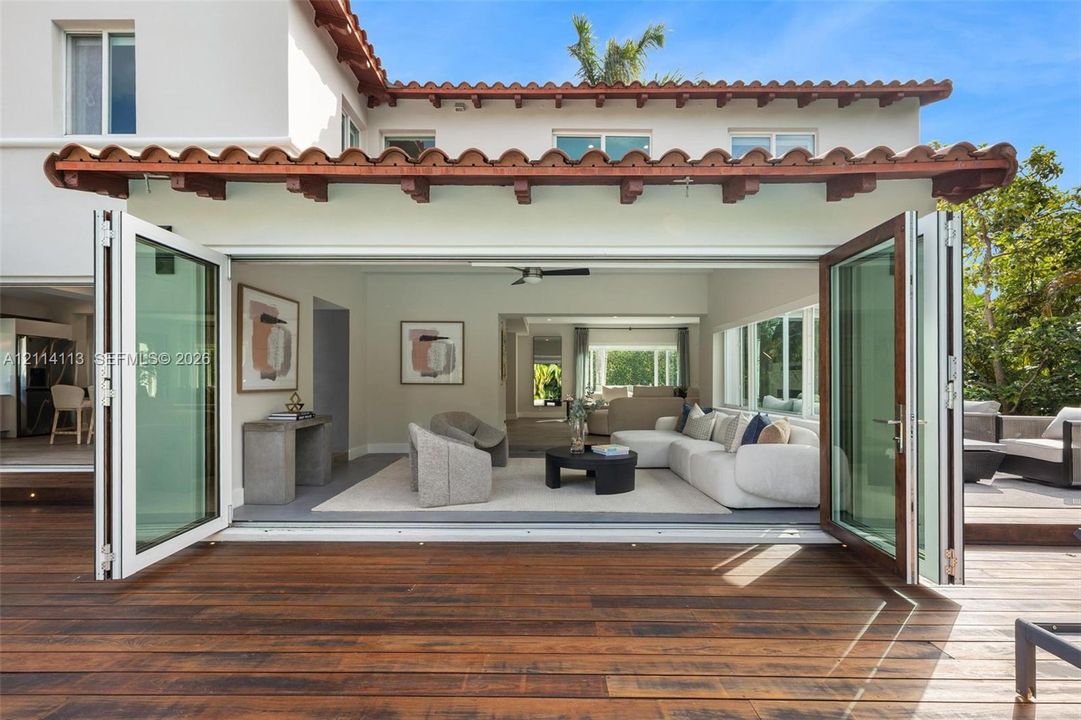 Stucco exterior featuring a clay tile roof, expansive wood decking, and multi-panel folding glass doors
