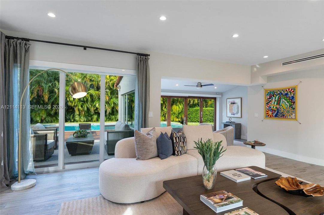 Living area featuring wood-finish flooring, recessed lighting, and multiple sliding glass door systems providing direct access to the outdoor pool area