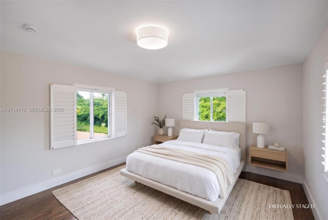 Room featuring wood-finish flooring, dual windows with plantation shutters, a neutral wall palette, and a circular flush-mount ceiling light