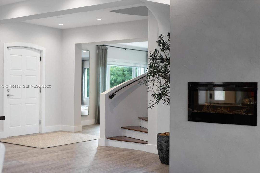 Foyer featuring recessed lighting, a recessed wall-mounted fireplace, a white arched-top entry door, and a staircase with wood-finish treads and a matte black handrail