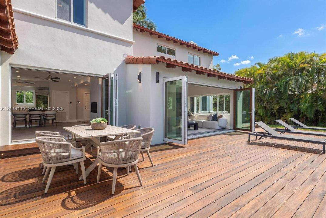 Expansive wood-finish deck with integrated bi-fold glass doors, white stucco exterior, and terracotta tile roofing
