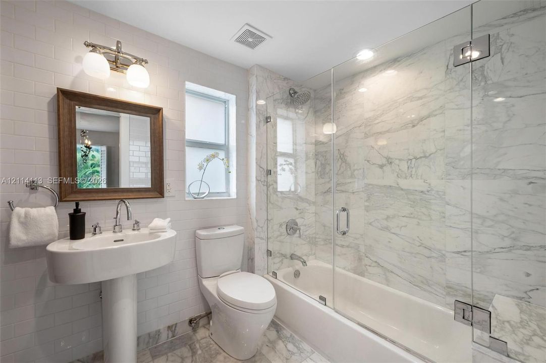 Full bathroom featuring a white porcelain pedestal sink, stone-patterned wall-to-wall shower surround with a frameless glass door, stone-patterned tile flooring, subway-tiled walls