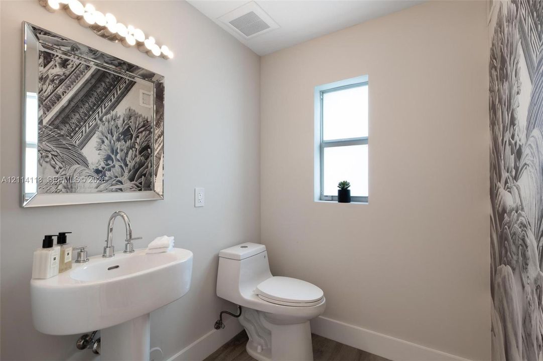 Pedestal sink with chrome faucet, multi-bulb vanity light, framed mirror, and toilet featuring a modern low-profile design