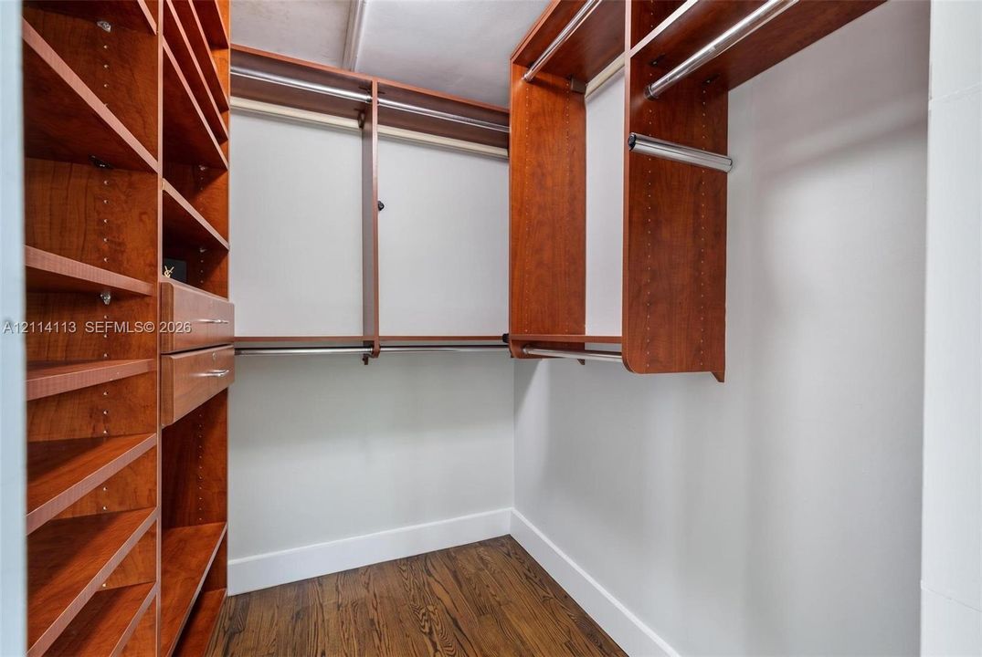 Walk-in closet featuring custom wood-finish shelving, integrated drawers, metal hanging rods, and wood-finish flooring