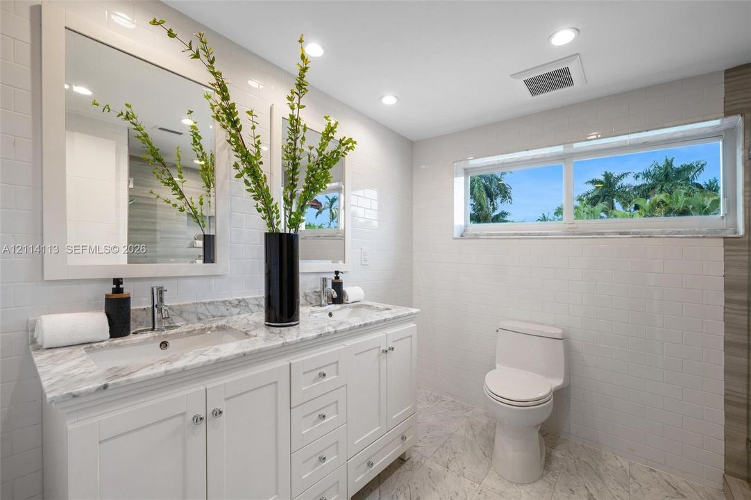 Double vanity with white cabinetry, stone-surface countertop, rectangular under-mount sinks, subway-tiled walls, and stone-finish flooring