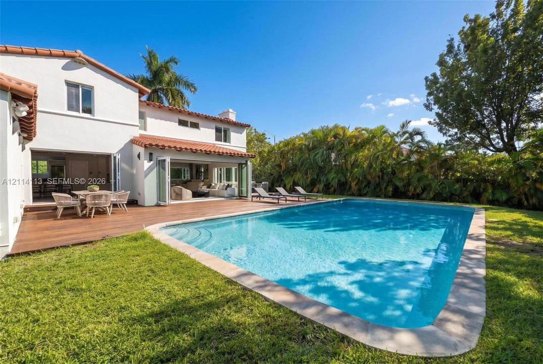 Stucco exterior with a clay tile roof, wood-finish decking, inground swimming pool, and folding glass wall systems