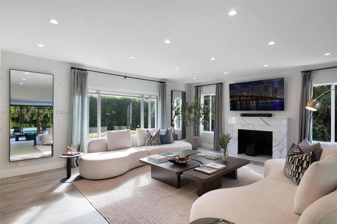 Spacious interior filled with natural light, featuring recessed lighting, stone-finish fireplace surround, large-format windows, and wood-finish porcelain flooring