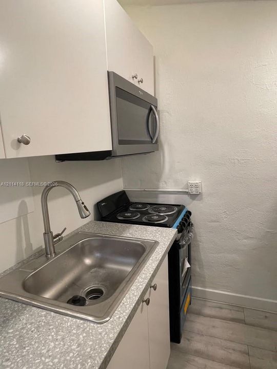 Kitchen featuring white cabinetry, a stainless steel sink with an arched pull-down faucet, a textured countertop, and a built-in microwave oven