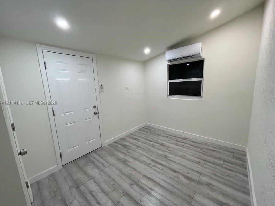 Interior space featuring wood-finish flooring, recessed lighting, wall-mounted climate control unit, and a single-hung window