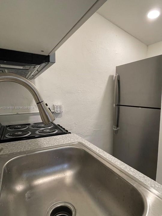 Stainless steel refrigerator, stainless steel undermount sink, gooseneck pull-down faucet, four-burner electric cooktop, and speckled-finish laminate countertops