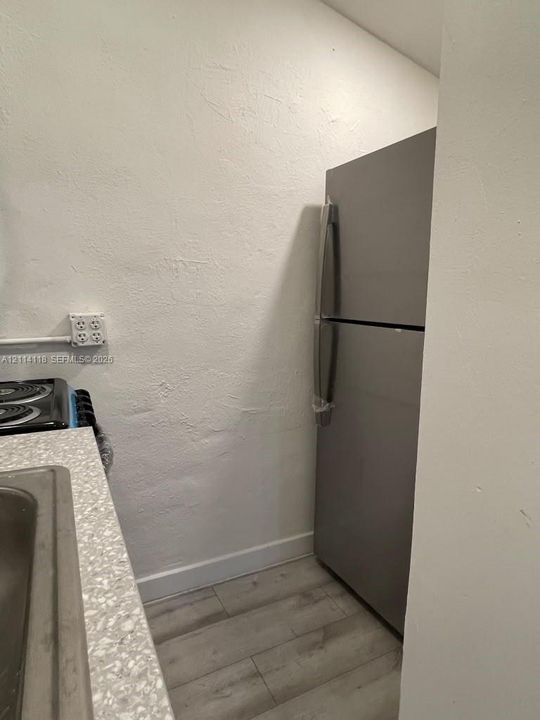 Stainless steel refrigerator, textured wall finish, speckled countertop, and wood-finish flooring
