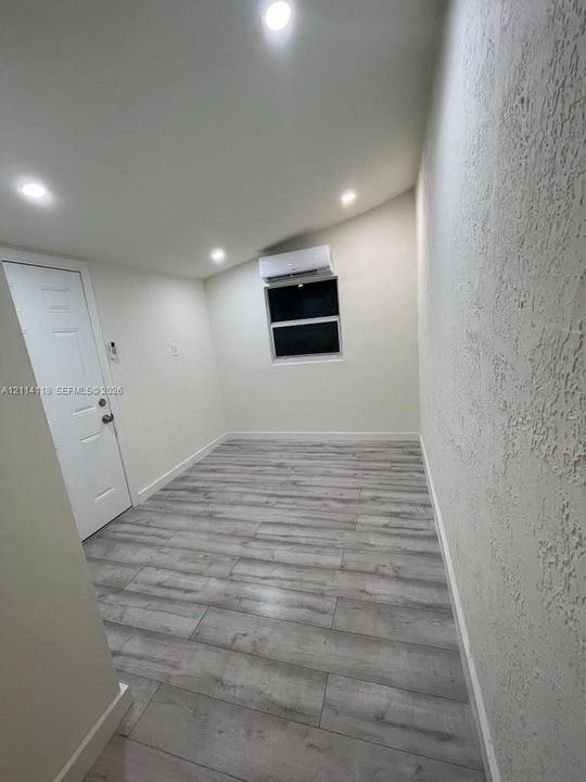 Interior room featuring wood-finish flooring, recessed lighting, a wall-mounted ductless mini-split unit, and a single-panel door