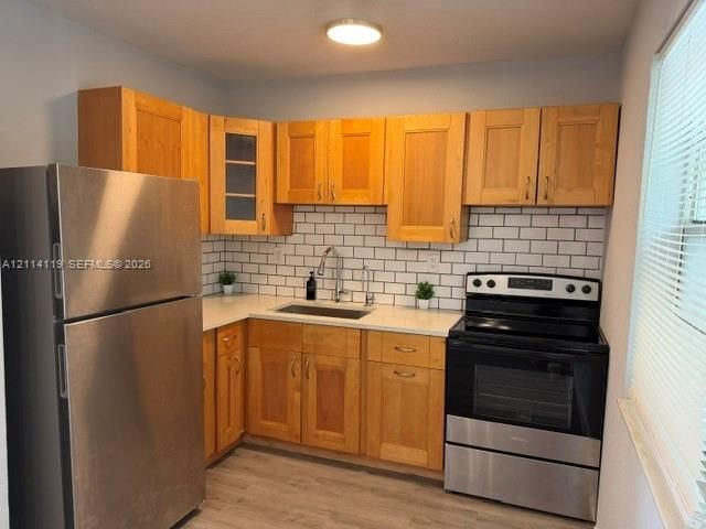 Kitchen featuring light wood-finish cabinetry, white subway tile backsplash, stainless steel appliances, solid-surface countertops, and wood-finish flooring