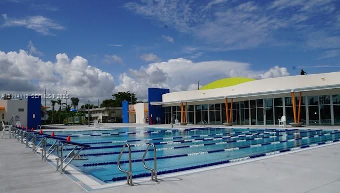 Multi-lane lap pool featuring metal starting blocks, stainless steel ladders, concrete decking, and floor-to-ceiling glass paneling