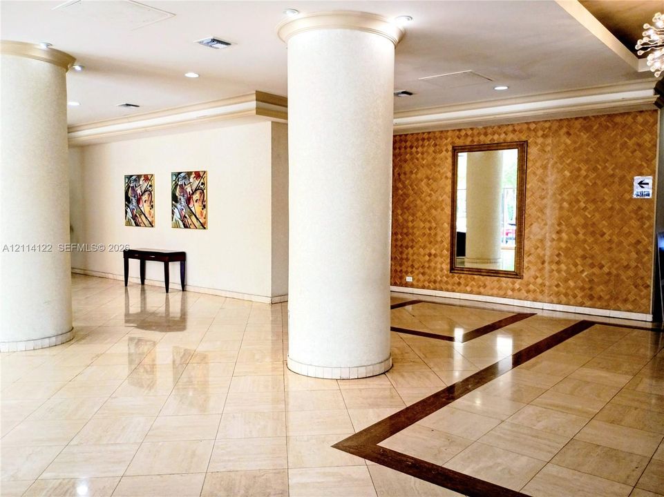 Spacious foyer featuring large-scale cylindrical architectural columns, polished stone flooring with decorative inlay, recessed ceiling lighting, and a textured accent wall