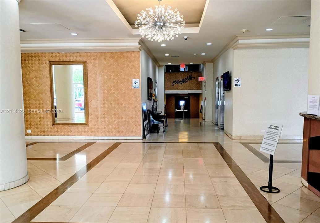 Lobby area featuring polished tile flooring with inlaid borders, a decorative recessed ceiling with a contemporary chandelier, and a textured accent wall