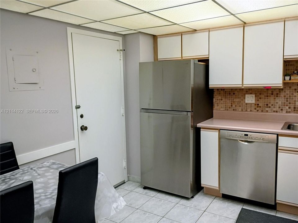 Kitchen area featuring stainless steel refrigerator and dishwasher, tiled backsplash, cabinetry with white finish, and tile flooring