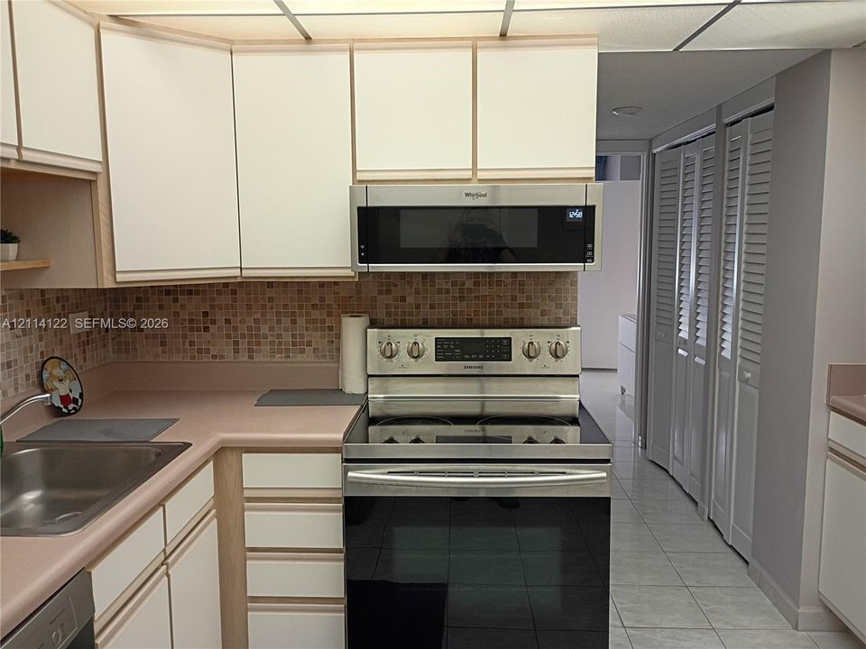 Kitchen featuring flat-panel cabinetry, stainless steel oven with range, matching over-the-range microwave, mosaic tile backsplash, and light-tone countertops