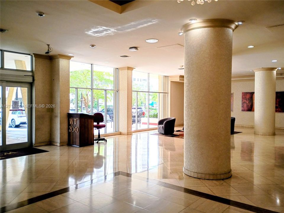 Lobby featuring floor-to-ceiling windows, polished stone tile flooring, structural columns, and recessed lighting