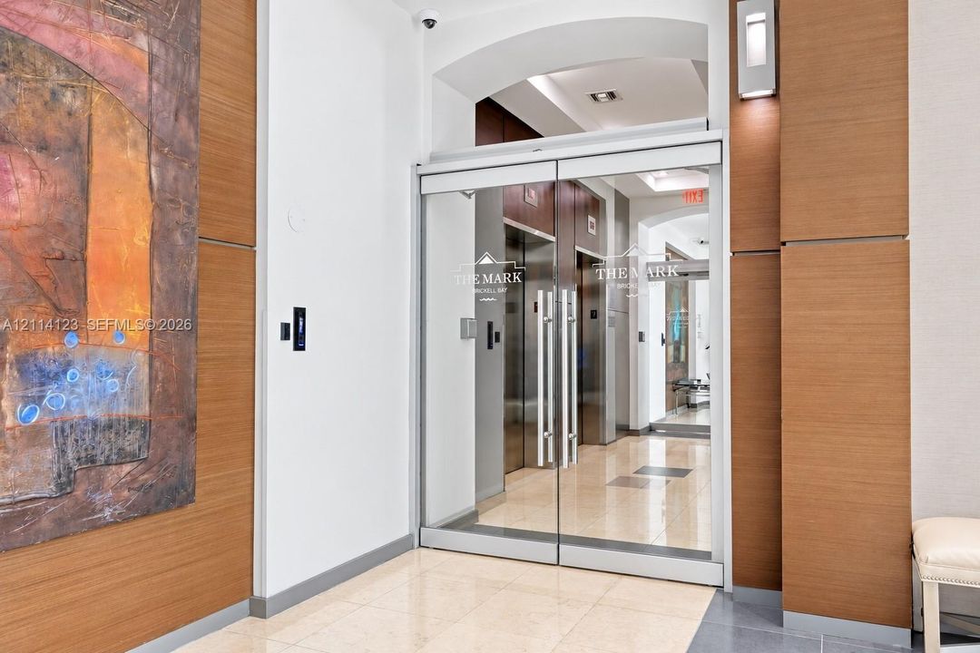 Entrance featuring glass double doors, polished stone flooring, wood-panel wall accents, and recessed wall-mounted sconces