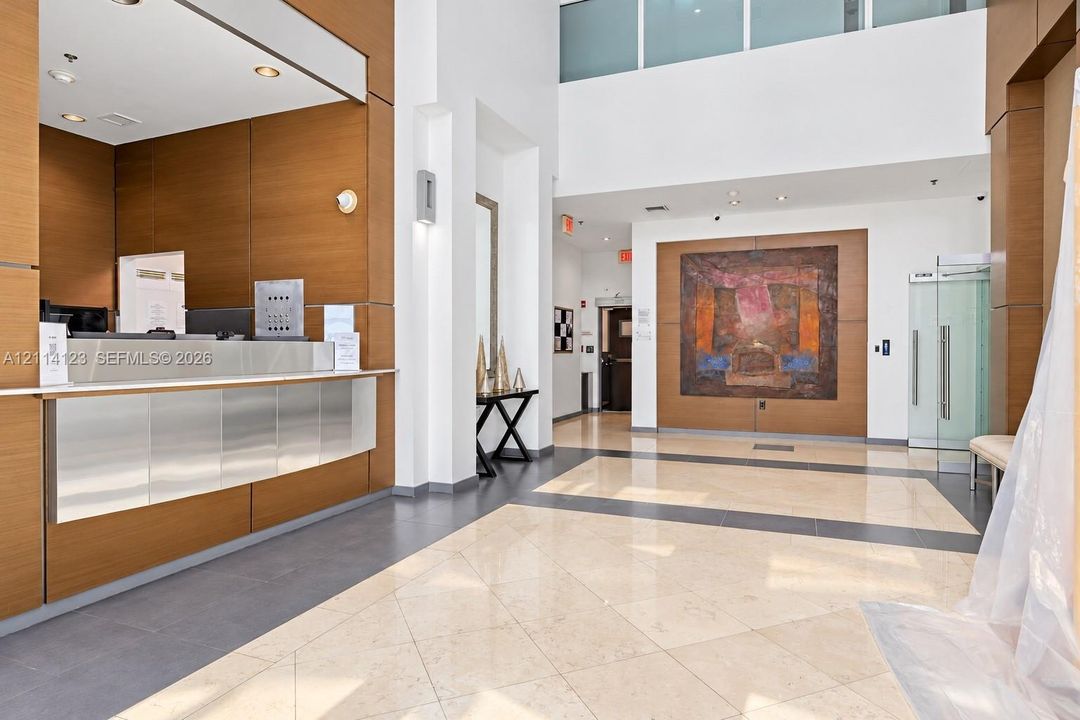 Lobby featuring double-height ceilings, wood-finish paneling, stone-tile flooring with decorative inlays, and a stainless steel reception desk