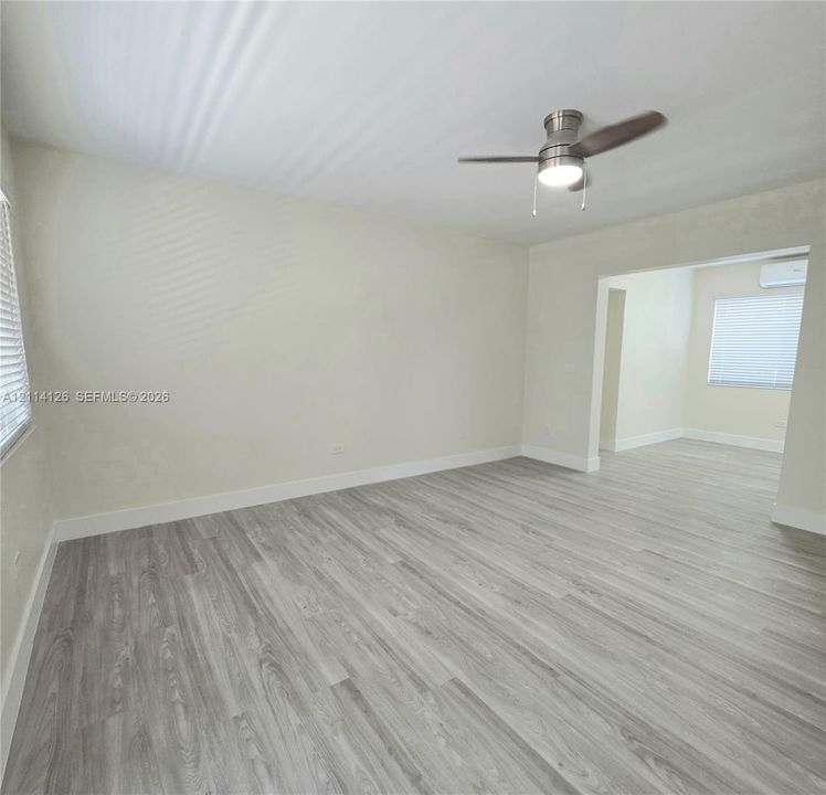 Neutral-toned interior space featuring wood-finish flooring, a contemporary ceiling fan with integrated lighting, and horizontal window blinds