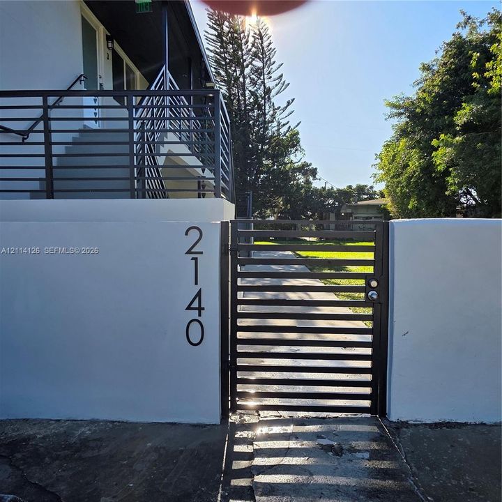 Stucco perimeter wall featuring a metal pedestrian gate, horizontal-slat metal railings, and modern vertical house numbering