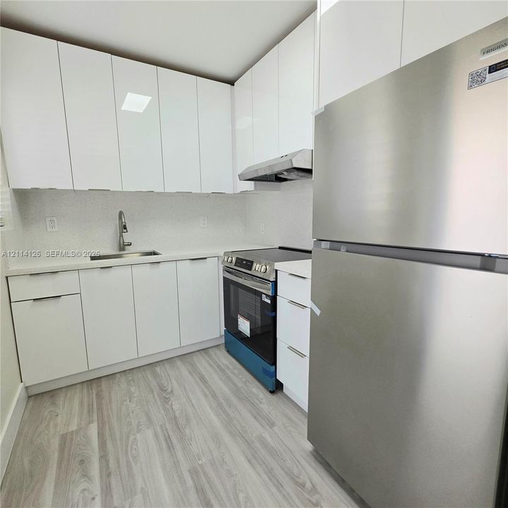 Kitchen featuring high-gloss white cabinetry, quartz countertops, stainless steel appliances, and wood-finish flooring