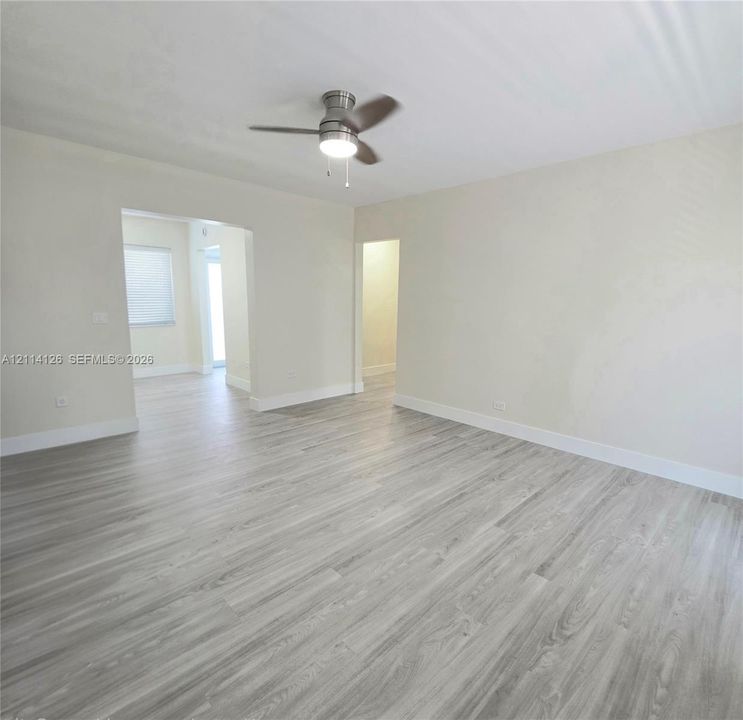 Neutral wall color, wood-finish flooring, and a ceiling-mounted light fixture with a fan