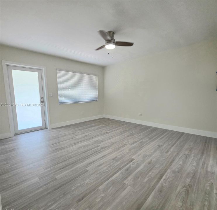 Room interior featuring wood-finish flooring, a neutral wall palette, a ceiling fan with integrated lighting, and a single-light exterior door