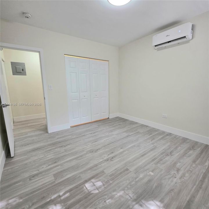 Wood-finish flooring, wall-mounted climate control unit, and closet featuring white paneled double doors