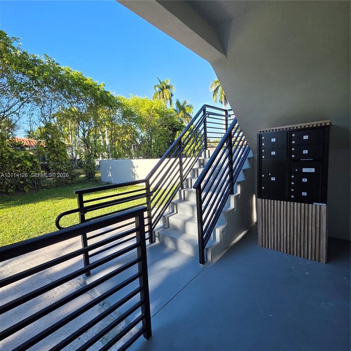 Exterior concrete staircase featuring black metal railings and a built-in parcel locker station with vertical wood-slat detailing